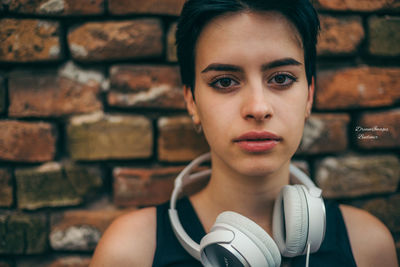 Close-up portrait of young woman against brick wall