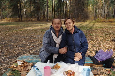 Elderly people have a picnic in a pine forest in autumn. they look optimistically at the camera.