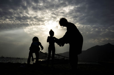 Silhouette friends standing on shore against sky during sunset