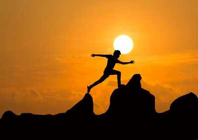 Silhouette man standing on mountain against orange sky