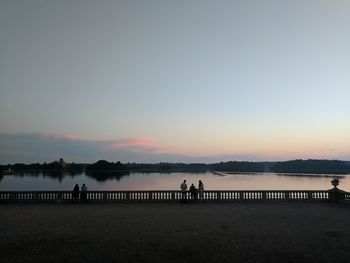 Silhouette people by river against sky during sunset