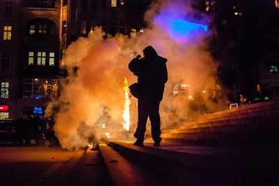 Rear view of silhouette man standing by fire on steps at night