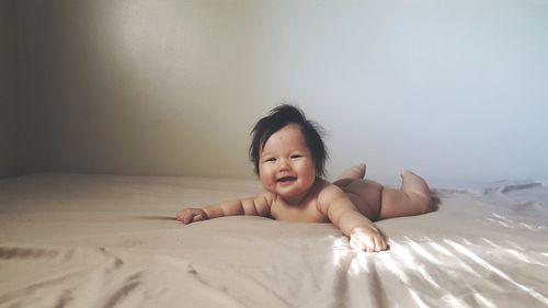 Portrait of smiling naked baby girl lying on bed at home