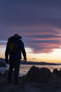 Rear view of man standing on rock at sunset