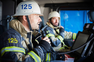 Firefighter talking on microphone while sitting with coworker in fire engine