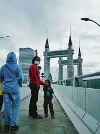Rear view of people walking on bridge against cloudy sky