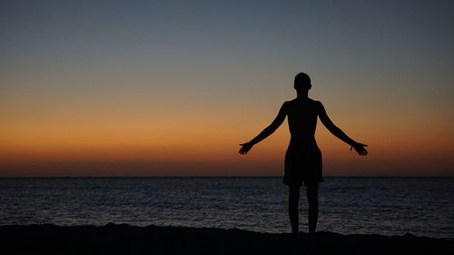 Silhouette woman standing at beach during sunset