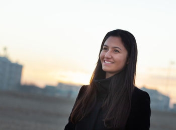 Portrait of smiling young woman standing against sky during sunset