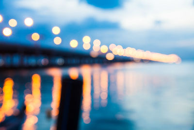 Defocused image of illuminated lights in sea against sky