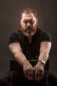 Portrait of man sitting against black background