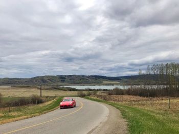 Red sports car on hillside road against sky