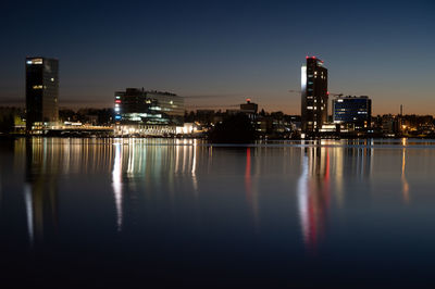 Modern financial district skyscrapers casting reflections on the water with vibrant color skies.