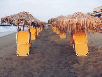 Yellow deck chairs with parasols at beach against sky