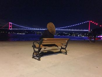 Rear view of woman sitting on suspension bridge at night