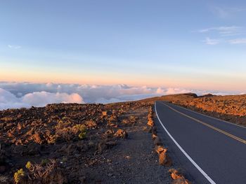 Road leading towards landscape against sky during sunset