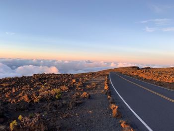 Road leading towards landscape against sky during sunset