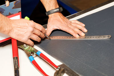 The male hands of the worker mark out a sheet of roofing iron with a pencil and a metal ruler. 