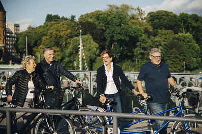 Cheerful senior male and female friends with bicycles on bridge