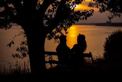 Silhouette man sitting on bench against sky during sunset