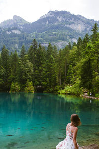 Rear view of woman standing by lake against mountain