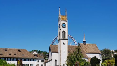 Low angle view of clock tower amidst buildings against clear blue sky