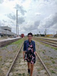Portrait of beautiful woman standing on railroad track against sky