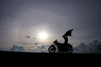Silhouette man with motorcycle on landscape against sky during sunset