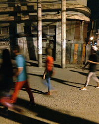 Blurred motion of people walking on street against buildings at night