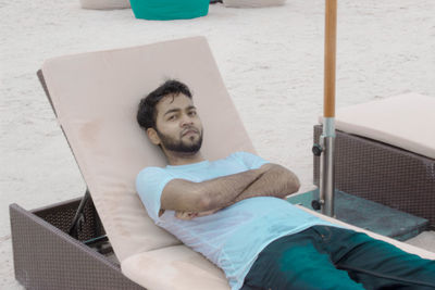 Portrait of young man relaxing on lounge chair at beach