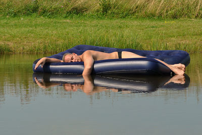 Shirtless man resting on pool raft in lake during sunny day