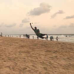 People playing on beach against sky during sunset