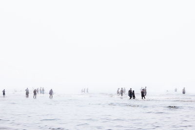 People standing in sea against clear sky