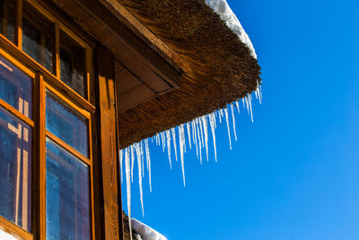 Icicles on edge of house roof with blue sky in the background