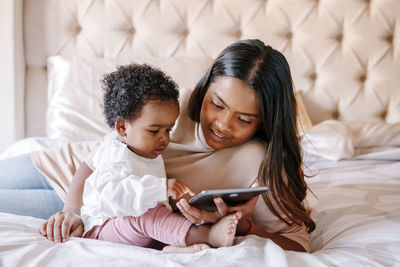 Mixed race indian black mother with toddler baby girl watching cartoons on tablet. ethnic diversity. 