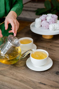 Midsection of woman's hands poring tea in cups.