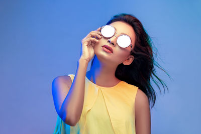 Portrait of smiling woman wearing sunglasses standing against blue background