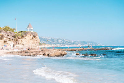 Lighthouse on beach by sea against clear sky