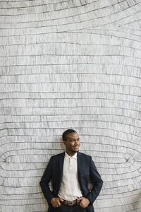 Smiling male professional standing with hands in pockets in front of wall