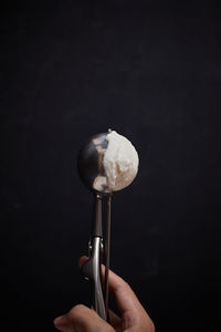 Cropped hand holding ice cream against black background