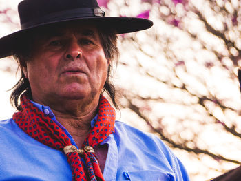 Portrait of senior man wearing hat while standing against tree