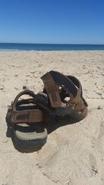 Close-up of shoes on sand at beach against clear sky