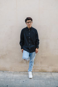 Young transgender man leaning on a wall while posing outdoors on the street.