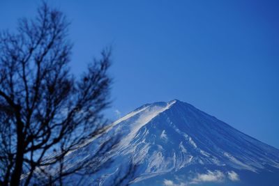 Low angle view of snow covered mountains against clear blue sky