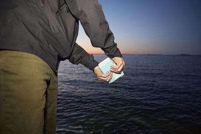 Mid section of person holding container at sea