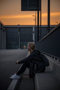 Woman sitting on railing against building during sunset