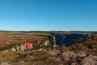 Rear view of man standing on rock against sky