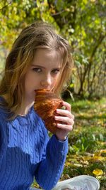 Girl in a blue sweater in the autumn forest has breakfast with a crispy croissant 