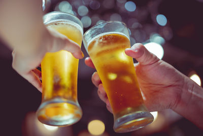 Cropped hands of people toasting beer glasses in bar