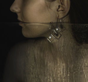 Silver geometric earring in grandfather's ear with a long neck on a background of glass with drops