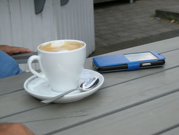 Coffee served by mobile phone on wooden table at outdoor cafe